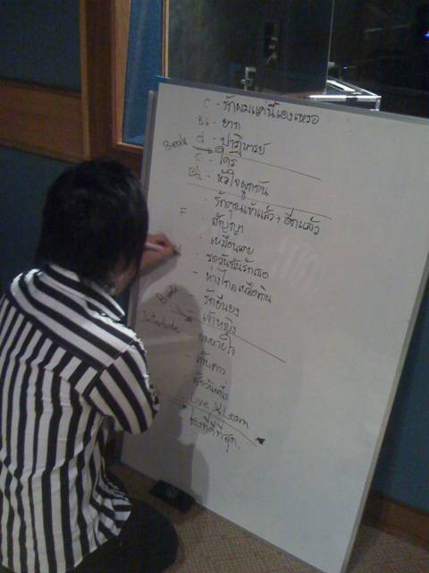 Natty กำลังเขียนคิวเพลง วิธีต่อเพลง และคีย์เพลงลงบน whiteboard ให้นักดนตรีดูระหว่างซ้อม